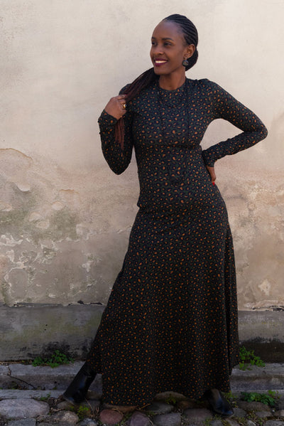 En lång klänning med långa ärmar, rund hals, fickor och klockad kjoldel som går till ankeln i leopard mönster på mörkgrön grund från märket Esther & Inez